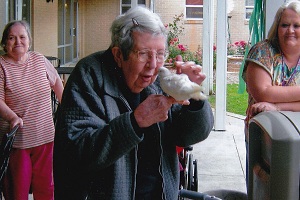 An Elderly patient is holding a bird and smiling.
